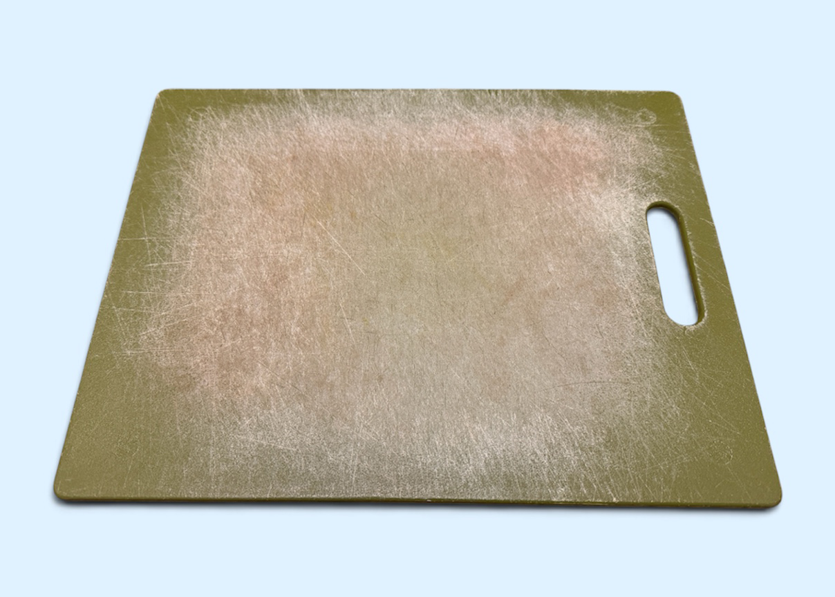 Green Plastic Cutting Board with Numerous Grooves from a Knife