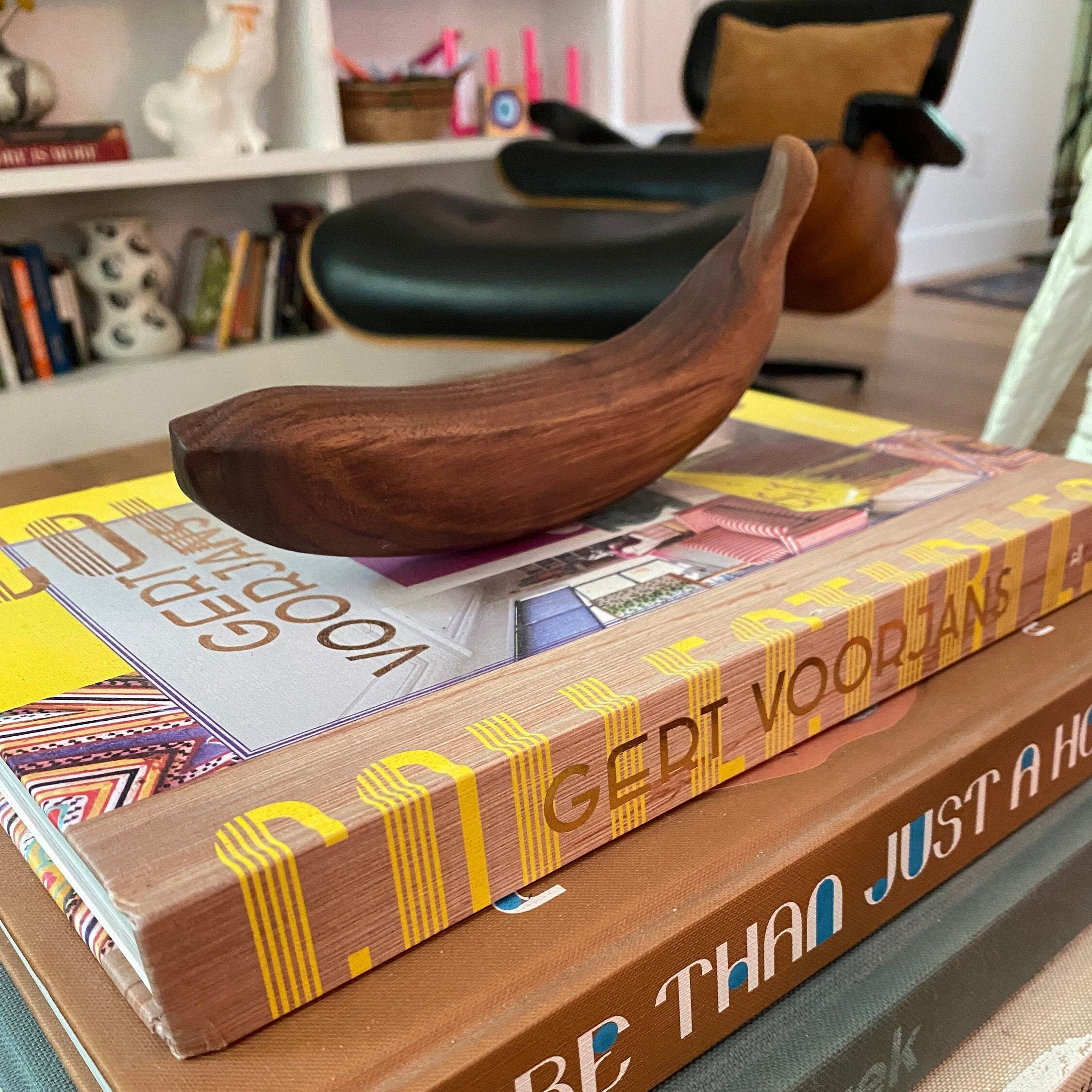 Stack of books with a wooden banana on top, in a room setting.