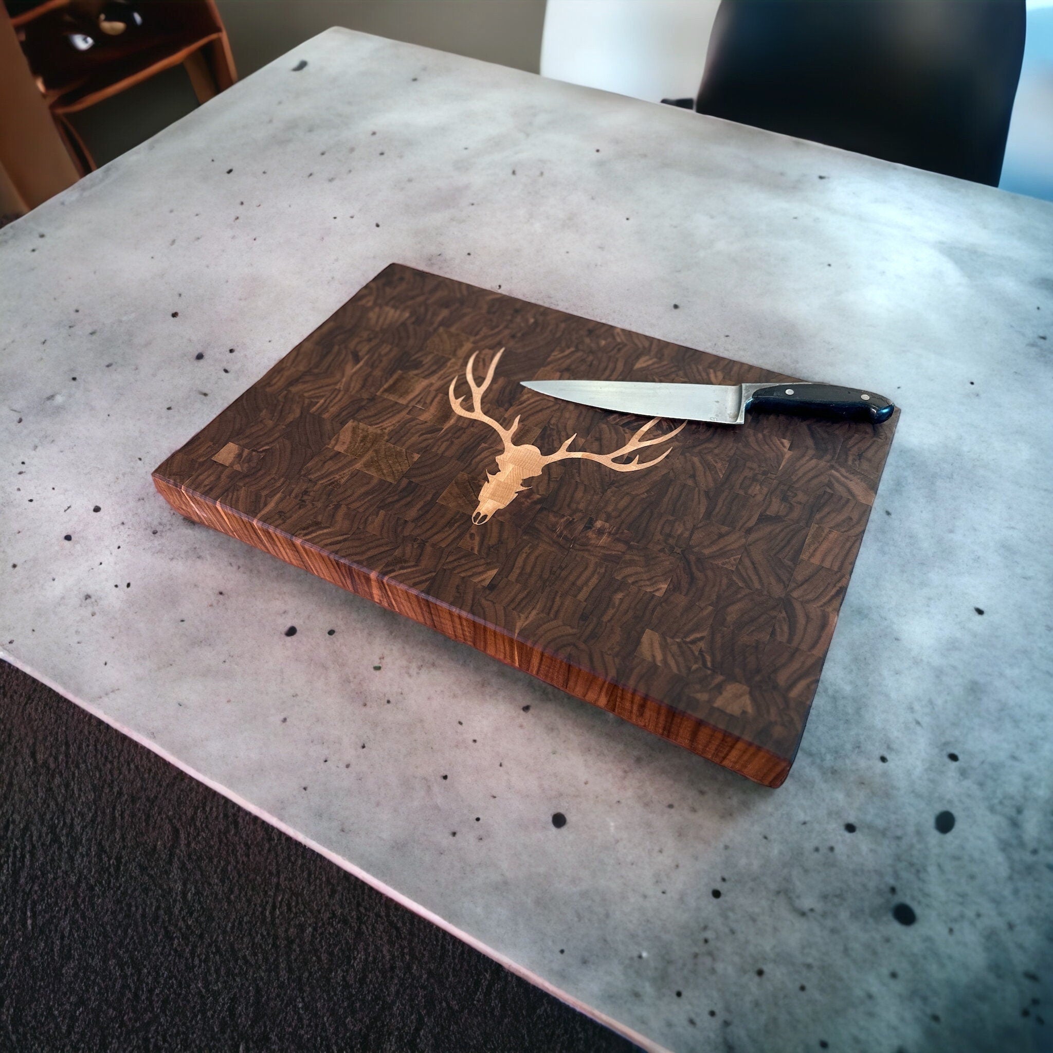 Wooden cutting board with deer design and knife on a speckled countertop