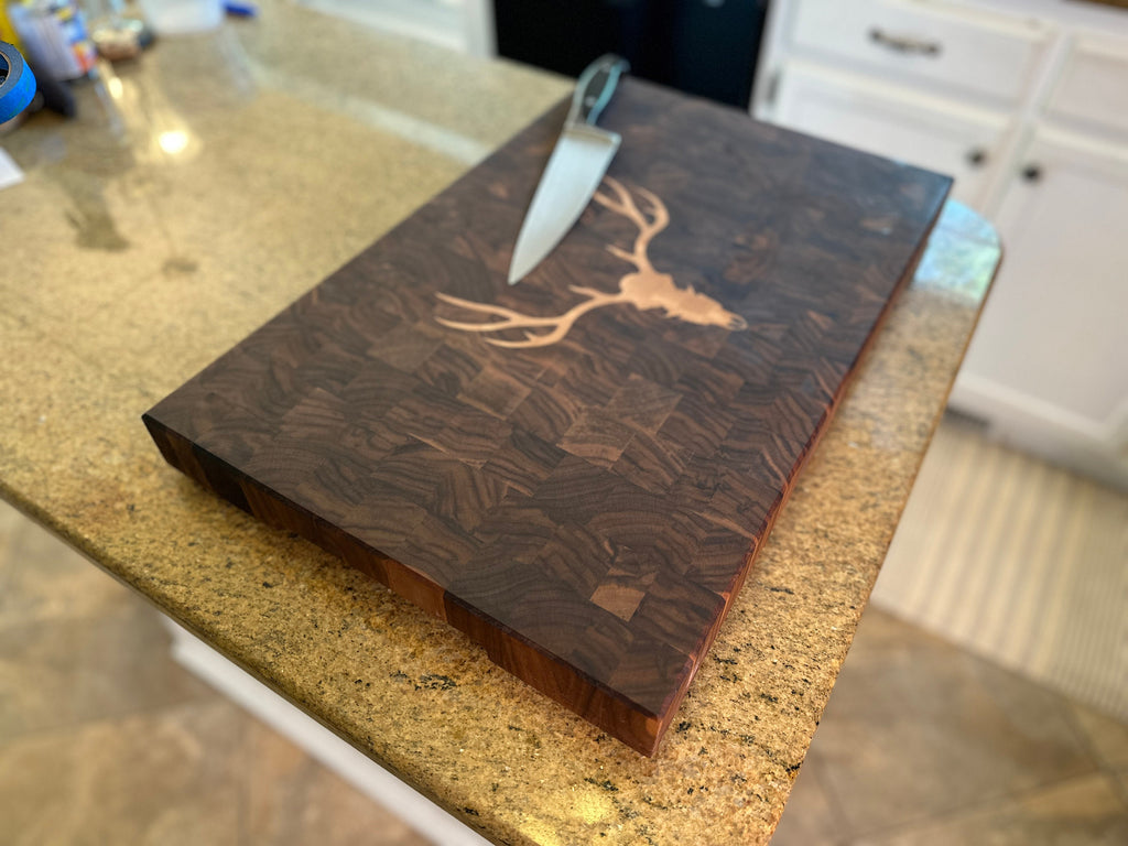 Wooden cutting board with engraved deer head design on a kitchen counter.