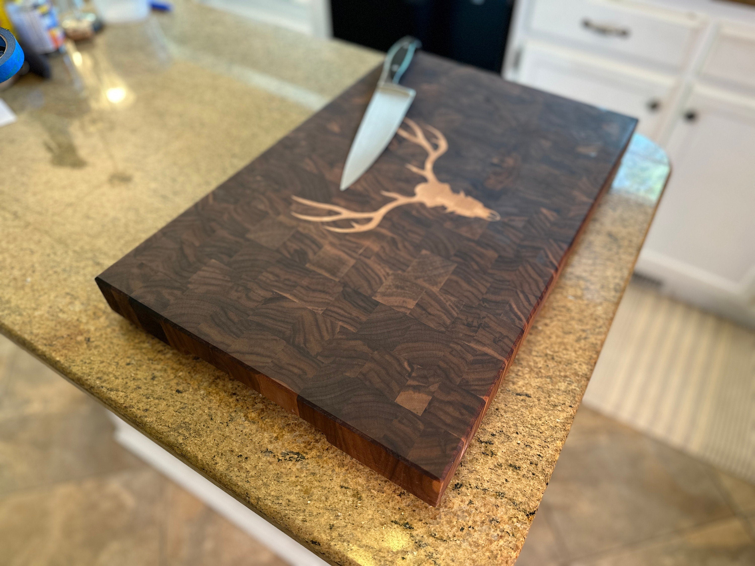 Wooden cutting board with engraved deer head design on a kitchen counter.