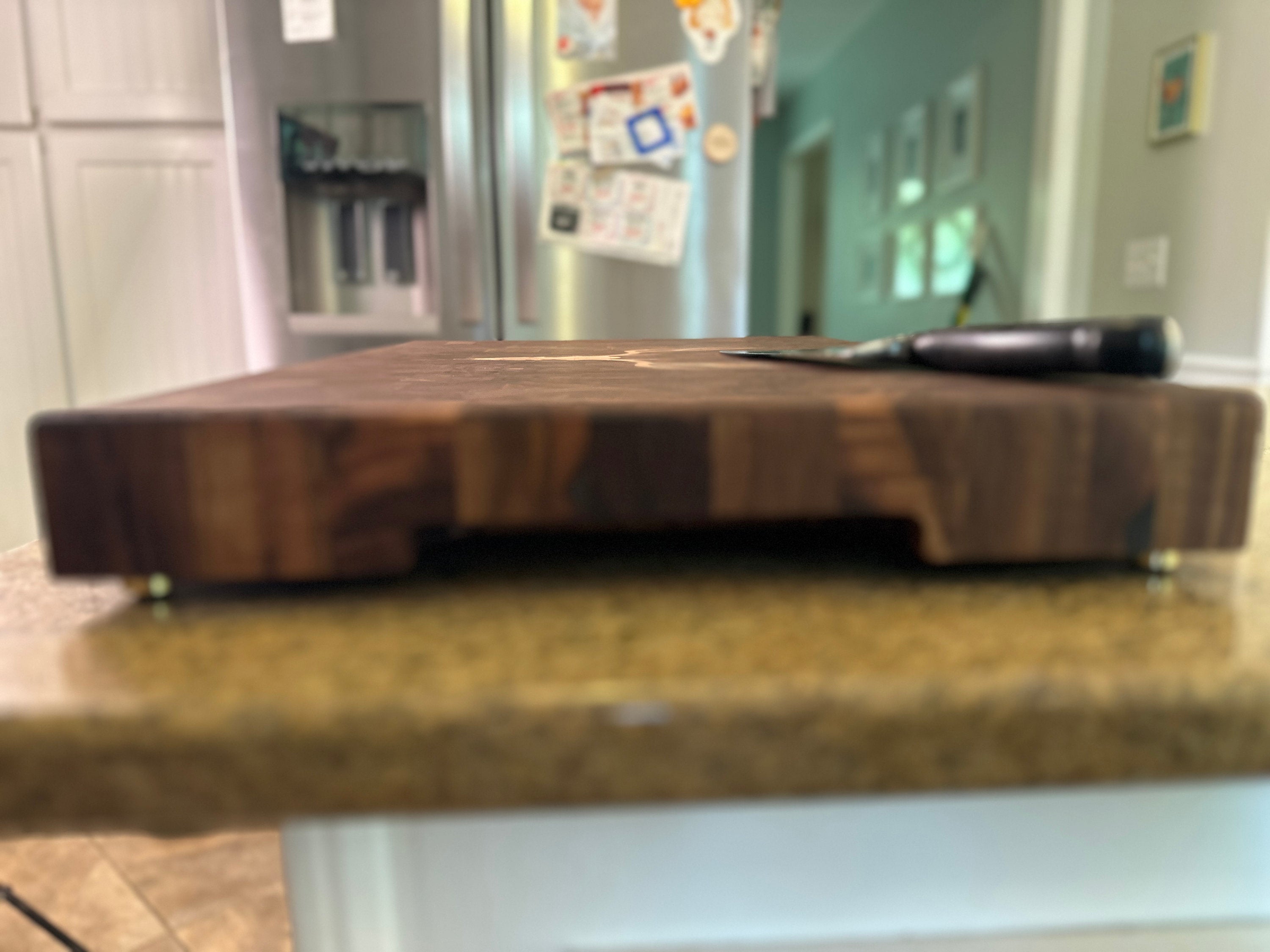 Wooden cutting board on a kitchen counter with a refrigerator in the background