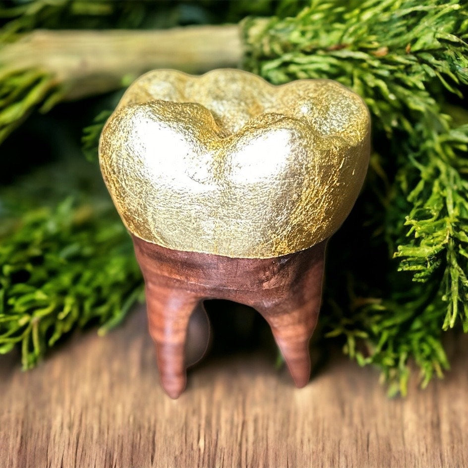Decorative tooth with gold crown on a wooden surface with green foliage