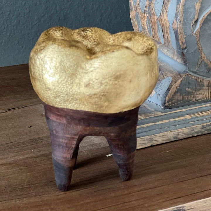 Decorative wooden tooth with gold cap on a wooden surface