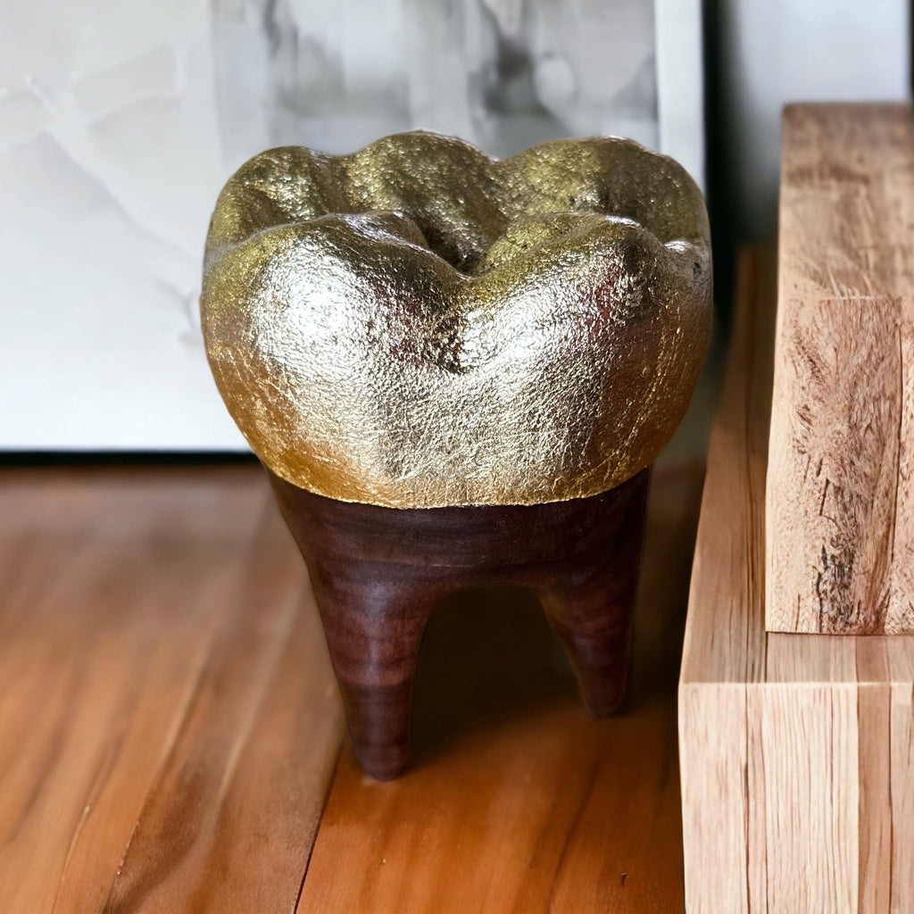 Decorative wooden tooth with a gold cap on a wooden surface