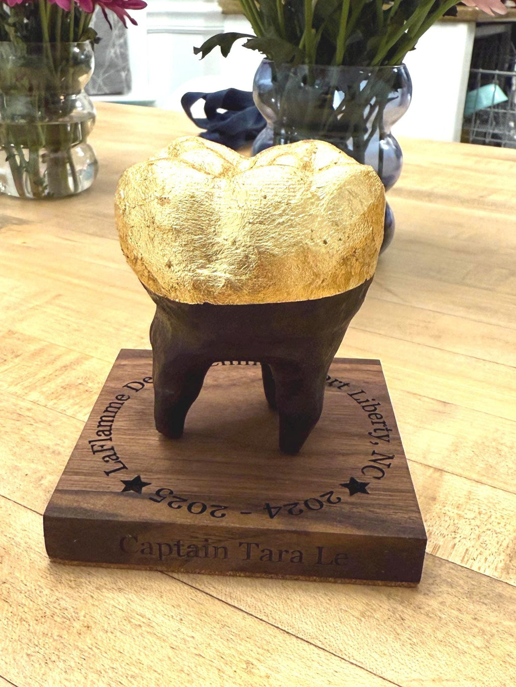 Decorative object resembling a tooth on a wooden base with engraved text, placed on a wooden surface.