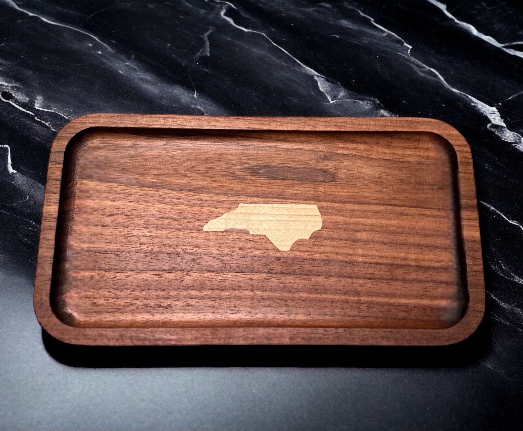 Wooden tray with an inlayed piece of wood depicting the state of North Carolina on a dark marble surface