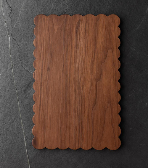 Wooden cutting board with scalloped edge on a dark stone background