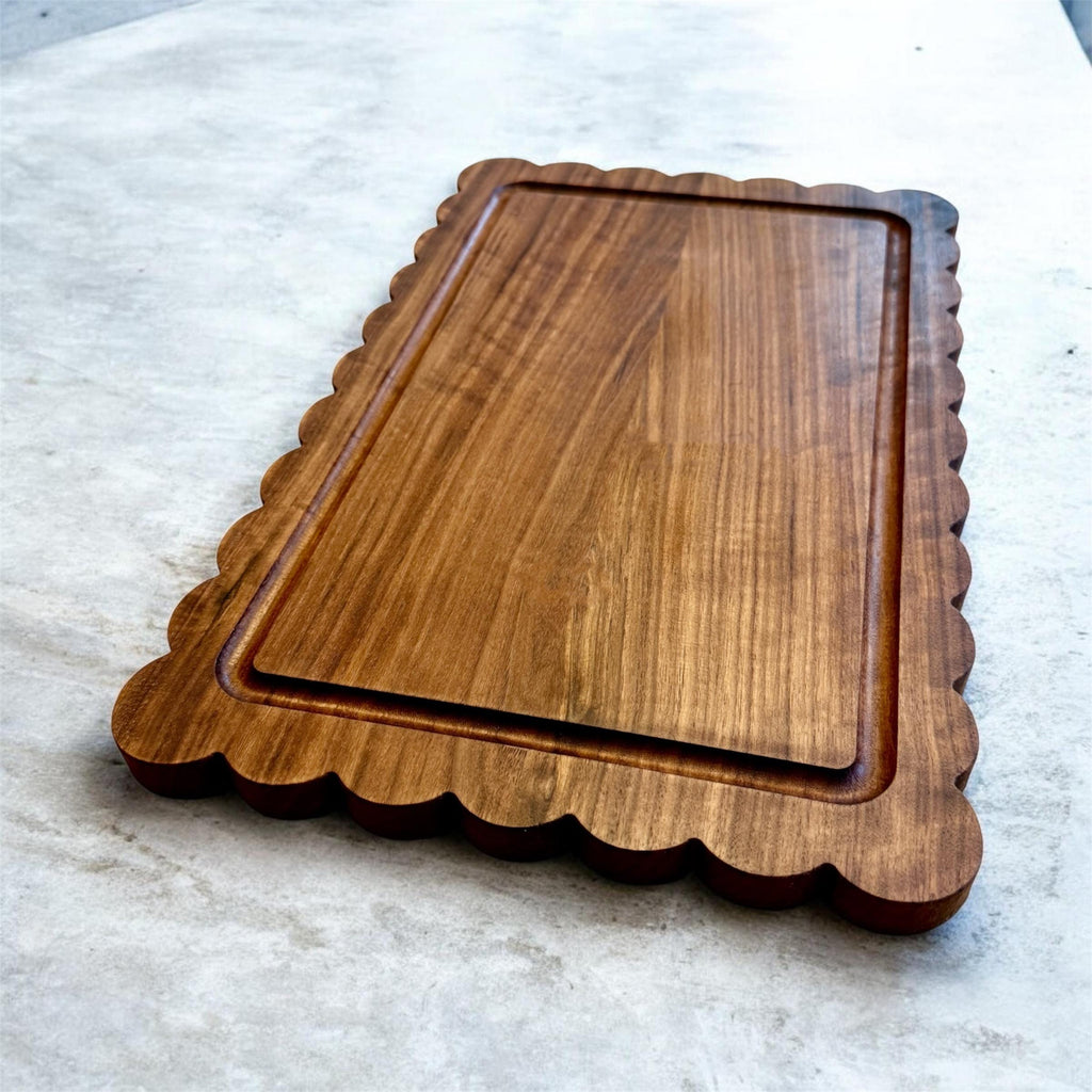 A wooden cutting board with scalloped edges and a juice groove on a light marble surface