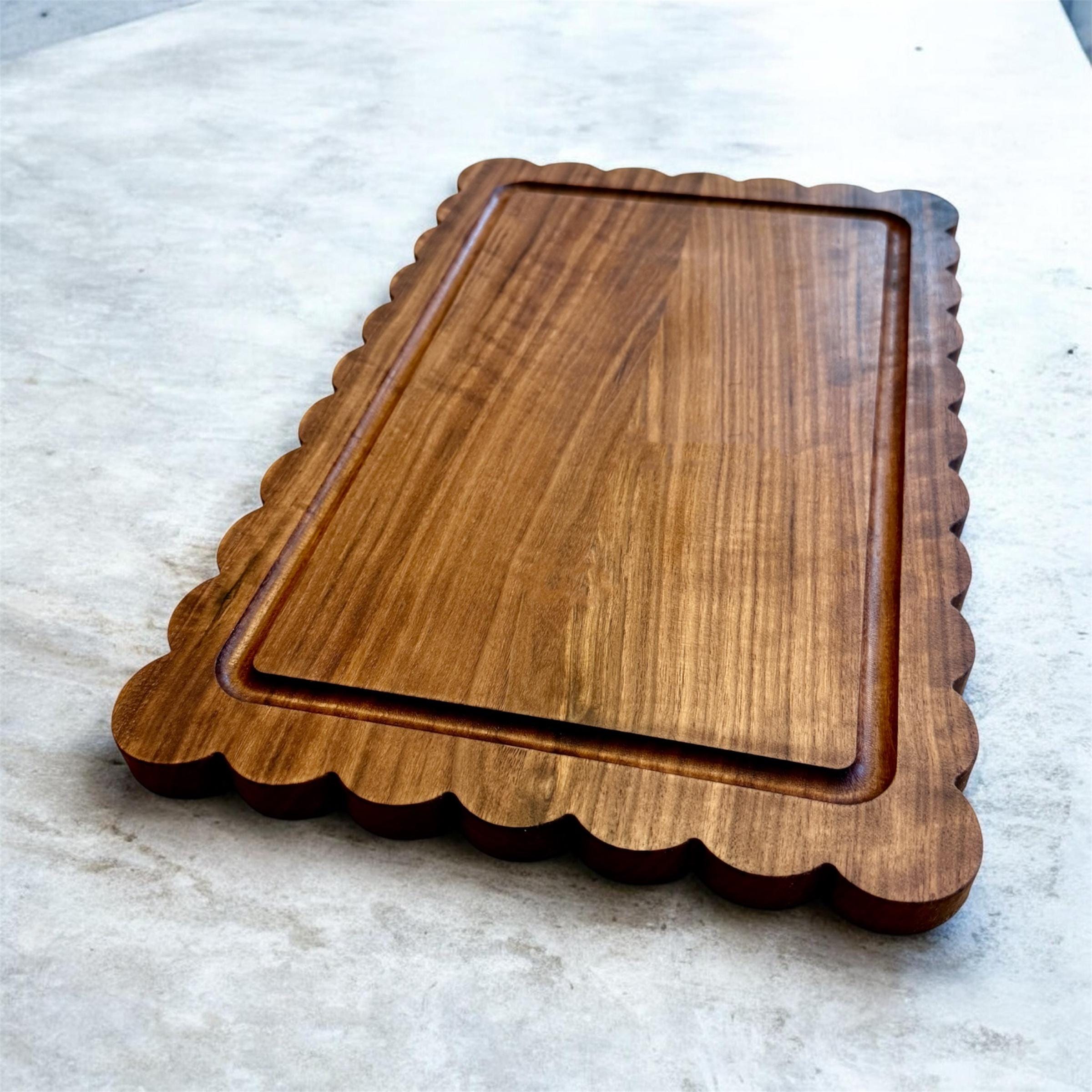 A wooden cutting board with scalloped edges and a juice groove on a light marble surface