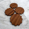 Four wooden coasters with scalloped edges on a marble surface