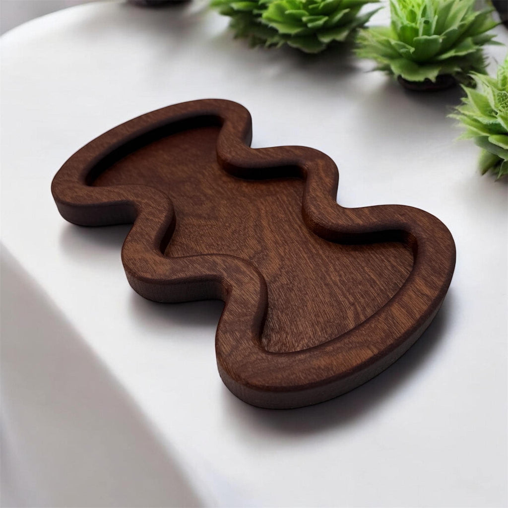 Wooden tray with a wavy design on a white surface with green plants in the background